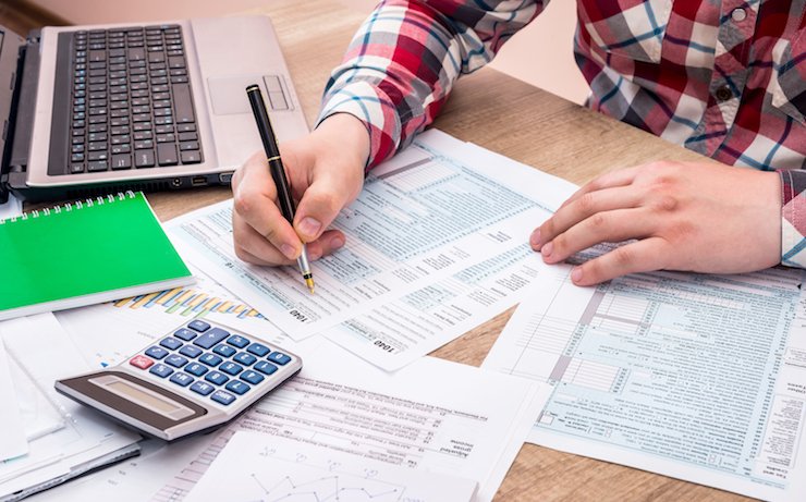 Man doing his taxes on paper near his laptop and a calculator