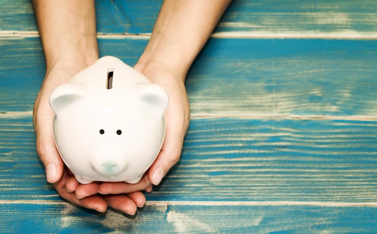 Persons hands holding white piggy bank on blue tinted wood table