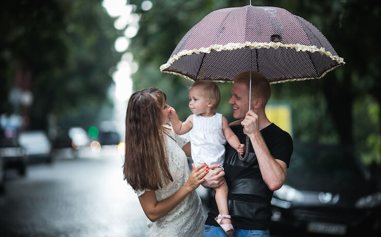 A happy family outside holding umbrella to protect from rain and sun