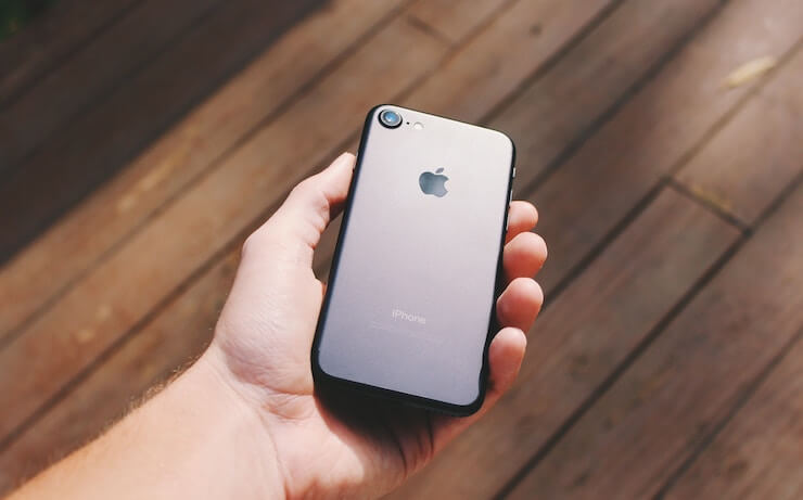 Man holding an iphone in the sun with wood floor in the background