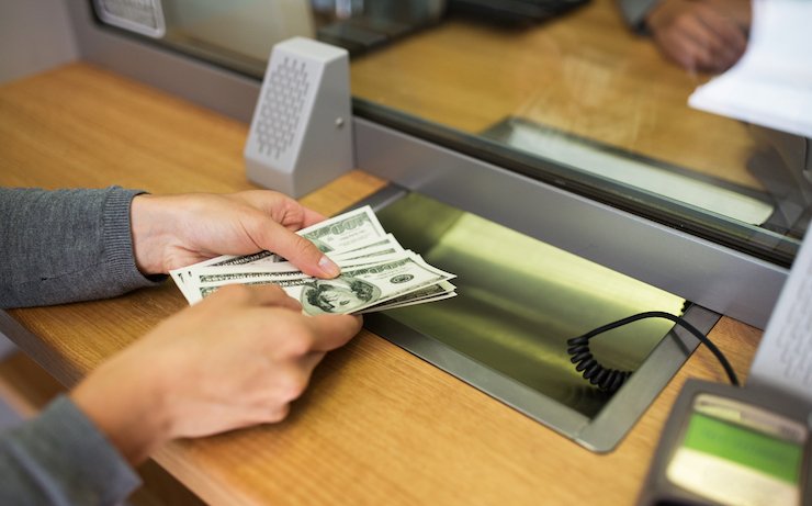 Woman withdrawing hundreds of dollars from bank teller at a bank