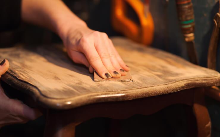 Person wearing black nail polish sanding a chair to refinish the wood surface